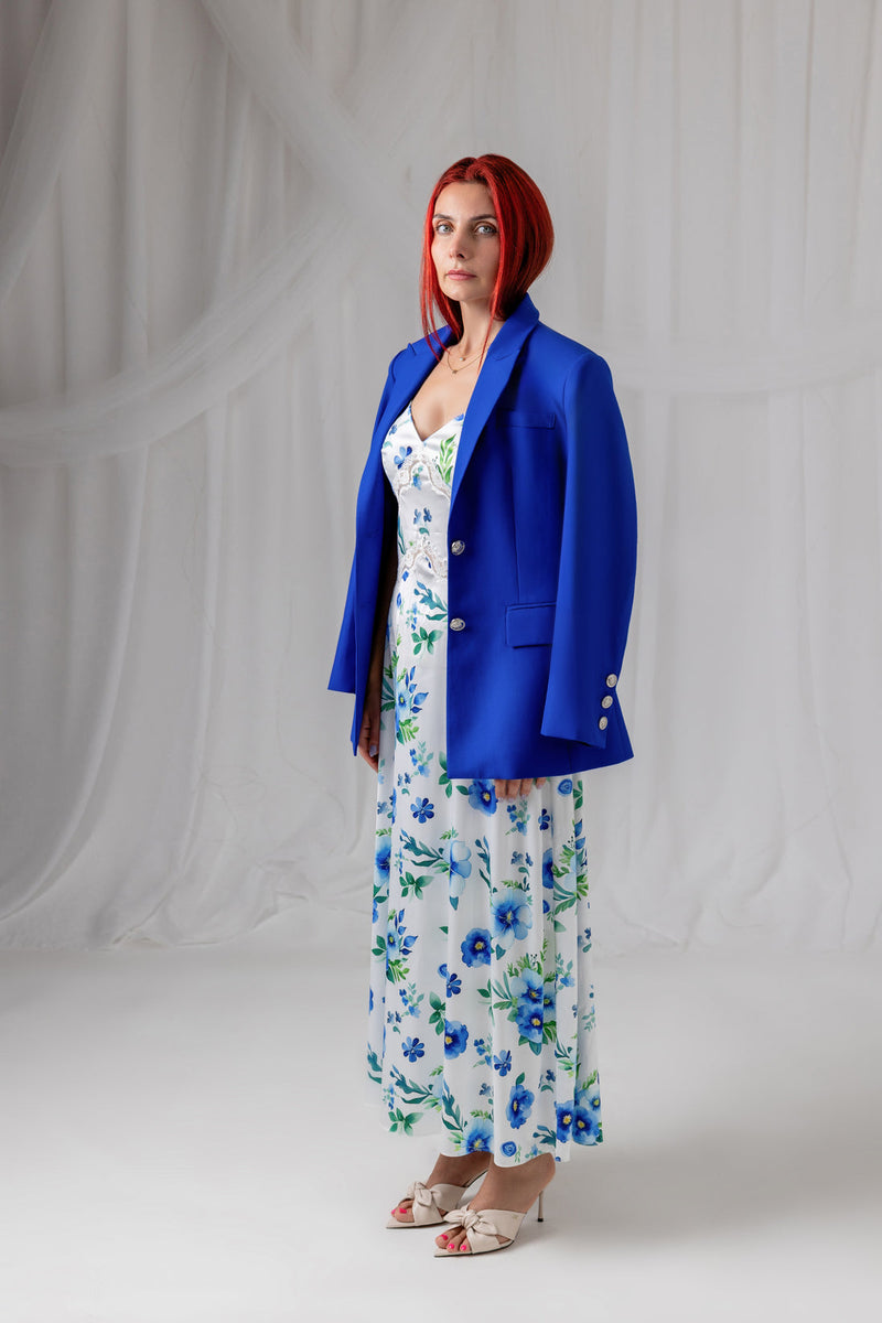 Model wearing the cobalt blue blazer with a floral maxi dress, three-quarter back view