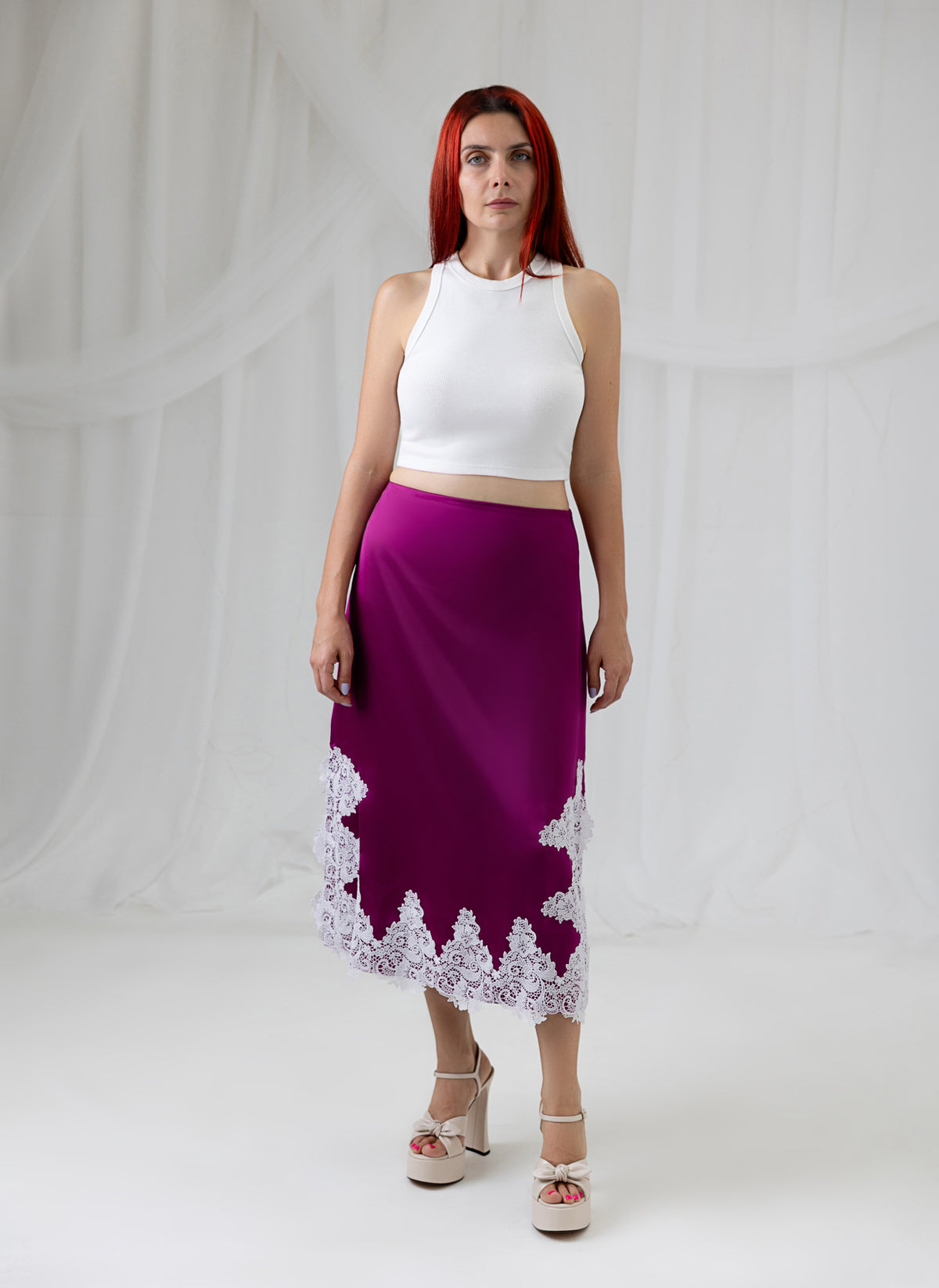 Model wearing the House of Lluvie' Burgundy Lace Whisper satin midi skirt with a white top, front view.