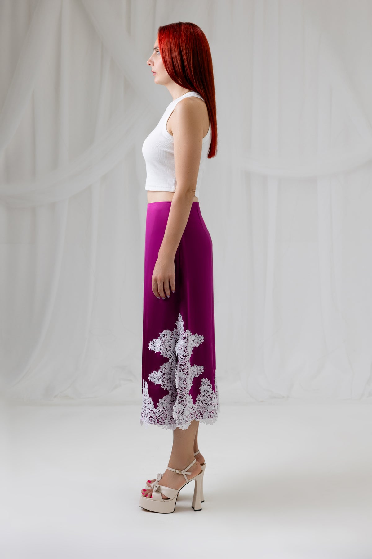 Model wearing the burgundy satin midi skirt with ivory lace hem, side view