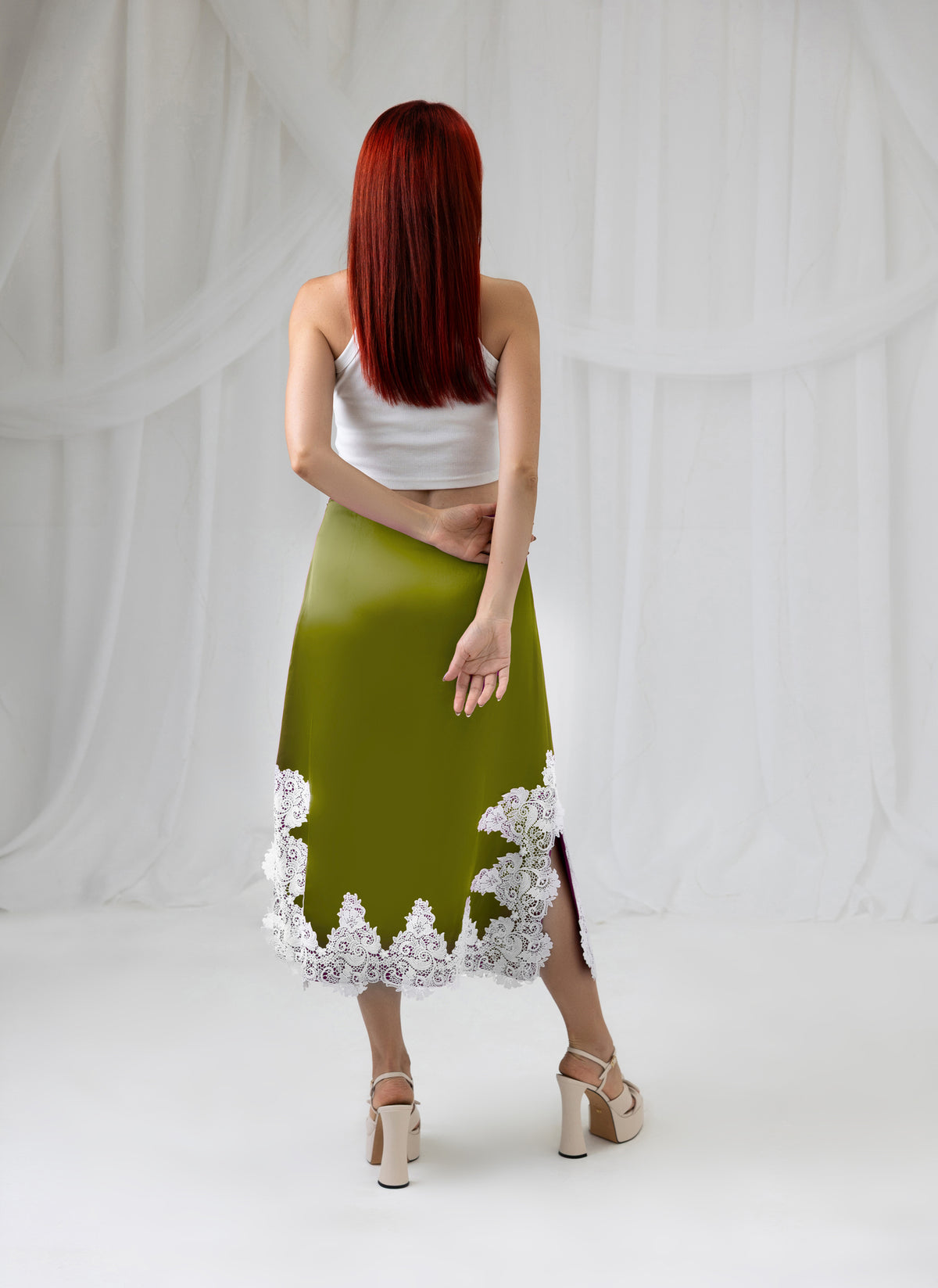 Model wearing the green satin midi skirt with ivory lace trim, back view