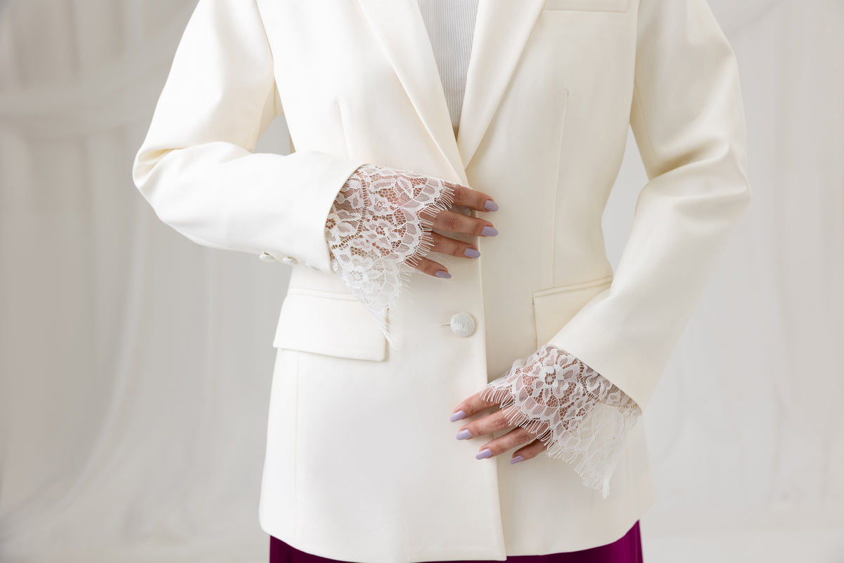 Close-up of the Ivory Muse Blazer sleeve cuff styled with a lace-trimmed burgundy skirt
